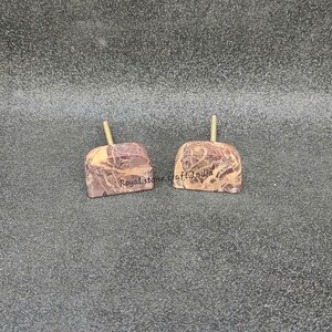 May include: Two stone apple-shaped objects with a light brown stem. The stone has a mix of brown and cream colors. The text "Royal stone craft India" is printed on the stone. The objects are on a gray surface.