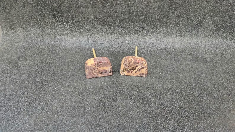 May include: Two stone apple-shaped objects with a light brown stem. The stone has a mix of brown and cream colors. The text "Royal stone craft India" is printed on the stone. The objects are on a gray surface.