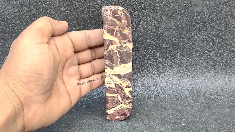 Front view of straight marble door handle held in hand, natural brown marble with golden veining showing real size and polished stone finish
