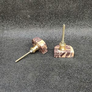 May include: Two decorative cabinet knobs with a brown and beige marbled stone design and brass hardware. One knob is lying on its side, while the other is upright. The text "i.India" is visible on the base of the upright knob.