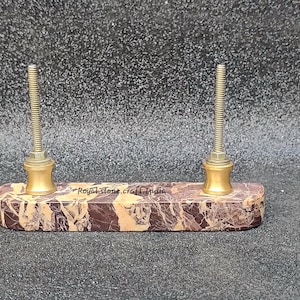 May include: A marble and brass pen holder with two threaded posts. The rectangular base features brown and tan veining. The text "Royal stone craft India" is visible on the base.