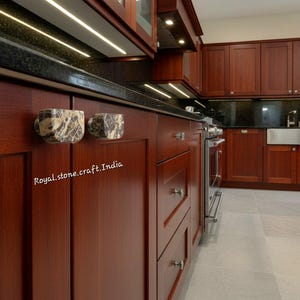 May include: A kitchen interior with dark wood cabinetry and a black countertop. Two decorative marble cabinet pulls are visible. The text "Royal.stone.craft.India" is printed on the cabinet. Stainless steel appliances and a light-colored floor complete the scene.