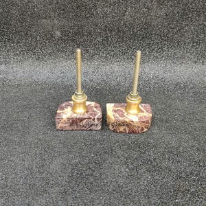 May include: Two decorative cabinet knobs. Each knob features a square, patterned stone base with a brass-colored metal accent and a threaded post. The stone base has a brown and white pattern. The knobs are for furniture.