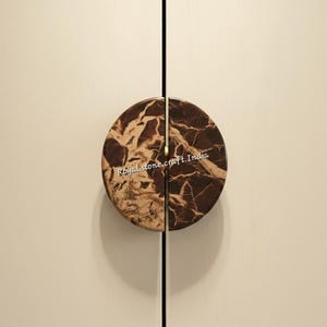 Può includere: Pomelli per ante di armadi con design circolare, divisi a metà con un motivo marmorizzato marrone e beige. I pomelli sono montati su un'anta di armadio beige chiaro. Il testo "Royal stone.craft.India" è visibile.