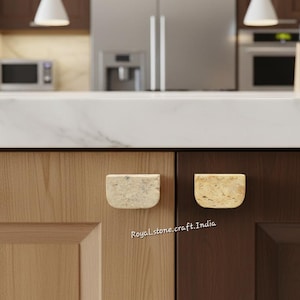 May include: Close-up of two kitchen cabinet doors with stone-like, half-moon shaped drawer pulls. One door is light wood, the other is dark wood. The countertop is white marble. The text "Royalstone.craft.India" is visible.