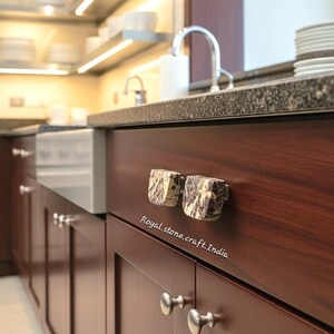 May include: Close-up of a kitchen cabinet with two square, patterned stone knobs. The cabinet is dark wood with a granite countertop. The text "Royal stone.craft.India" is visible.