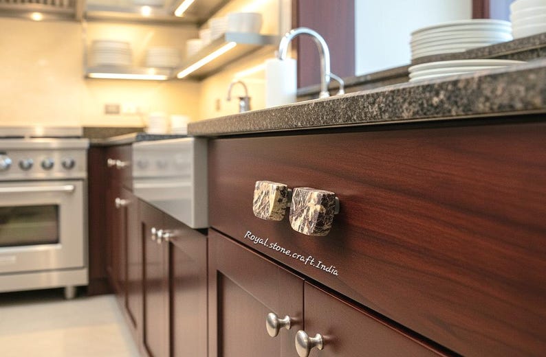 May include: Close-up of a kitchen cabinet with two square, patterned stone knobs. The cabinet is dark wood with a granite countertop. The text "Royal stone.craft.India" is visible.