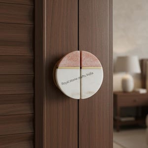 May include: A round door handle with a split design, featuring pink and white marble sections separated by a gold accent. The handle is mounted on a dark brown wooden door, with the text "Royal stone crafts India" visible.