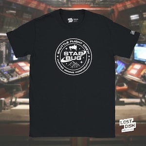 May include: Black t-shirt with a white circular graphic that reads "Shuttle Flight Crew Star Bug Jupiter Mining Corporation." The shirt has a crew neck and short sleeves. The Lost Dish Archive logo is in the bottom right corner.