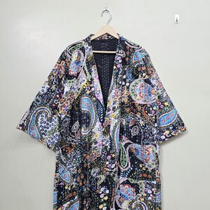Könnte beinhalten: Eine schwarze, kurzärmelige Kimono-Jacke mit einem lebendigen Paisley-Muster in Blau-, Gelb-, Rosa- und Grüntönen. Die Jacke hängt an einem Holzbügel vor einem neutralen Hintergrund. Die Jacke hat einen V-Ausschnitt.