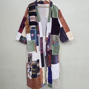 May include: A patchwork robe in a variety of colours and textures. The robe is made of different fabric squares, including velvet, and features a long, open design with pockets. The colour palette includes shades of brown, green, blue, and white.