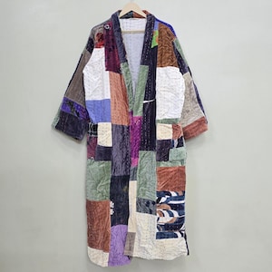 May include: A patchwork kimono-style robe with a variety of colors and textures. The robe is made of different fabric squares in shades of purple, brown, green, and blue. It hangs on a wooden hanger against a neutral background.