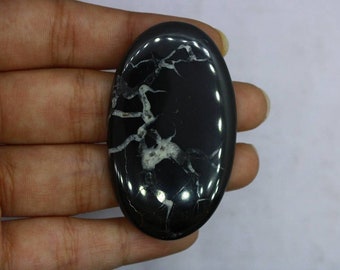 May include: A black and white oval cabochon gemstone with a dendritic pattern. The stone has a smooth, polished surface.