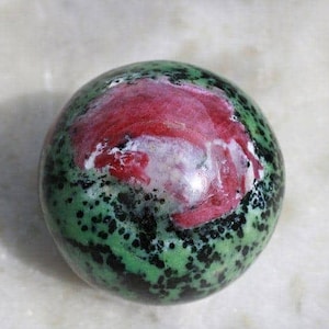 Könnte beinhalten: Eine grüne und rote Kugel mit schwarzen Flecken. Die Kugel ist aus poliertem Stein.