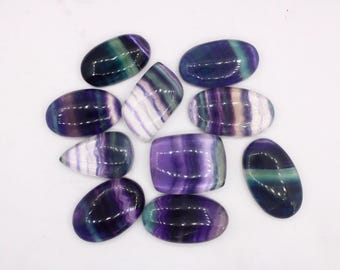 May include: A collection of ten polished fluorite cabochons in various shades of purple, green, and white. The cabochons are oval and teardrop shaped.