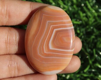 May include: A smooth, oval-shaped agate stone with a beautiful pattern of orange, white, and brown bands.