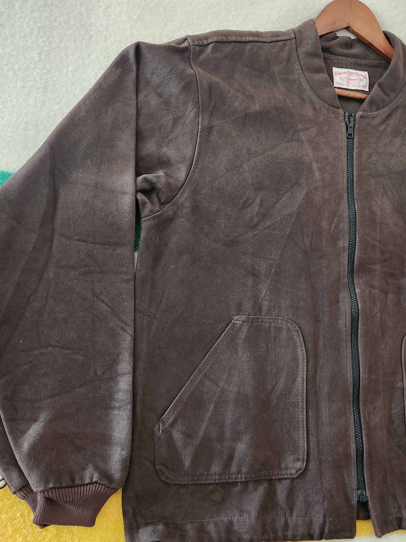 Peut inclure: Veste de bombardier marron avec une fermeture &eacute;clair noire et deux poches avant. La veste a un poignet c&ocirc;tel&eacute; et une &eacute;tiquette sur le col int&eacute;rieur. La veste est faite d'une mati&egrave;re douce semblable &agrave; du daim.