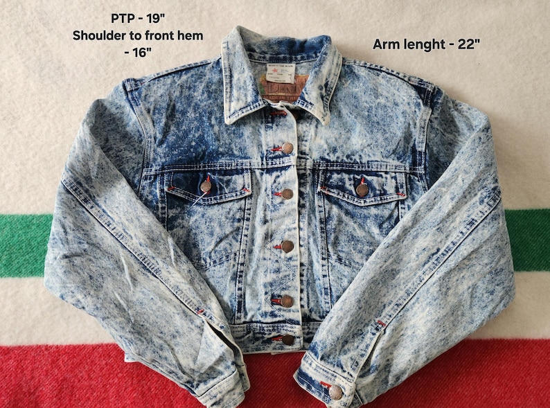 May include: Acid wash denim jacket with button fastenings, two chest pockets, and two side pockets. The jacket has a collar and long sleeves. PTP - 48 cm, shoulder to front hem - 41 cm, arm length - 56 cm.