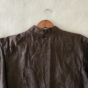 Peut inclure: Veste marron avec un col officier, suspendue &agrave; un cintre en bois. La veste a une fermeture &agrave; bouton unique au col et est faite d'un tissu textur&eacute;. Les manches sont longues et la veste semble &ecirc;tre de style d&eacute;contract&eacute;.