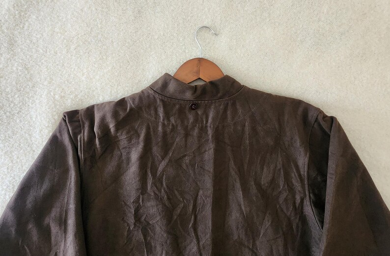 Peut inclure: Veste marron avec un col officier, suspendue &agrave; un cintre en bois. La veste a une fermeture &agrave; bouton unique au col et est faite d'un tissu textur&eacute;. Les manches sont longues et la veste semble &ecirc;tre de style d&eacute;contract&eacute;.