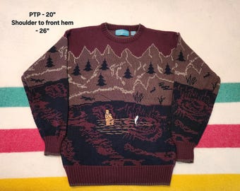 May include: A burgundy, brown, and navy blue knit sweater with a landscape design. The sweater features a mountain range, trees, and a fisherman. The shoulder to front hem measures 26 inches.