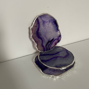 May include: Two purple agate coasters with silver trim. The coasters are stacked on top of each other.
