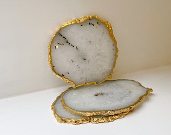 May include: Three white agate coasters with gold-painted edges. The coasters are stacked on top of each other.