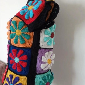 May include: A colorful crocheted top with a floral pattern. The top is made of squares with different colored flowers in each square. The flowers are in shades of red, blue, green, yellow, orange, and white.