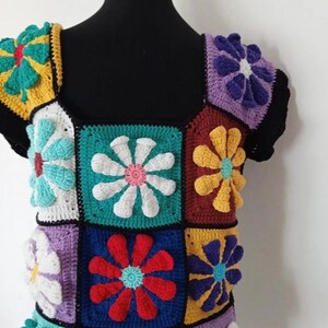 May include: A colorful crochet top with a square pattern of flowers in various colors, including red, yellow, blue, green, purple, and white.