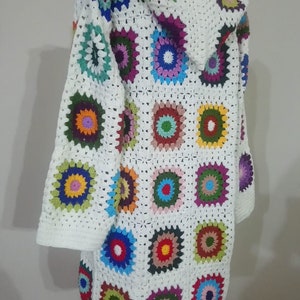 May include: White crochet cardigan with a hood, featuring colorful granny square motifs. The cardigan has long sleeves and a loose fit.