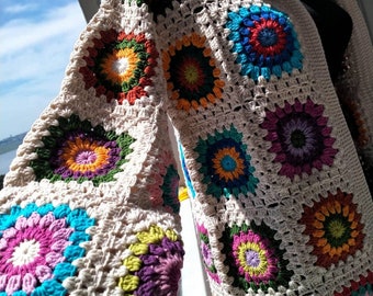 May include: A crocheted cardigan with a hooded neckline. The cardigan is made of beige yarn and features colorful granny squares with a circular pattern.