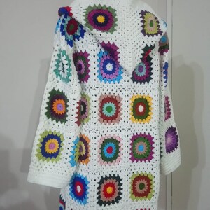 May include: White crochet cardigan with a hood, featuring a colorful granny square pattern. The cardigan has long sleeves and a loose fit.