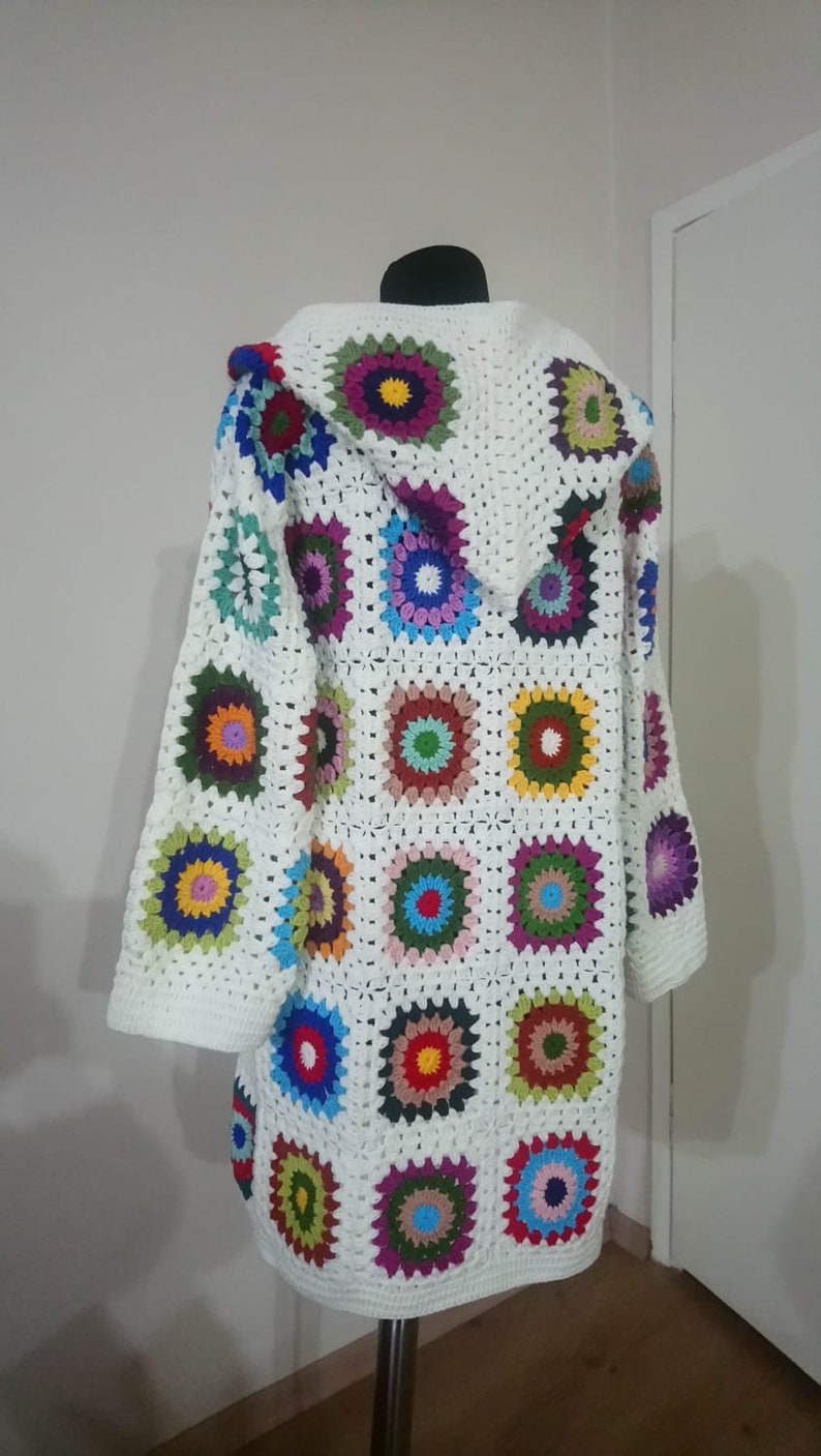 May include: White crochet cardigan with a hood, featuring a colorful granny square pattern. The cardigan has long sleeves and a loose fit.