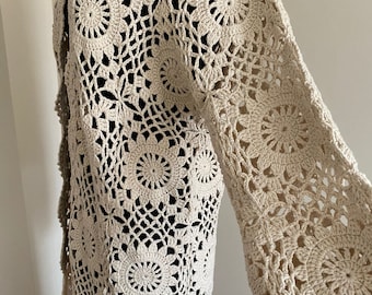 May include: A cream-colored crochet cardigan with a long, open front and long sleeves. The cardigan is made with a delicate, lacy pattern.