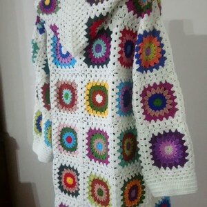 May include: White crochet cardigan with a hood, featuring a colorful patchwork design of granny squares with multi-colored circles in the center.