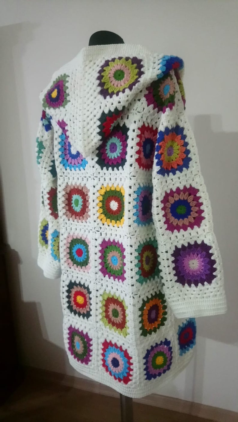 May include: White crochet cardigan with a hood, featuring a colorful patchwork design of granny squares with multi-colored circles in the center.