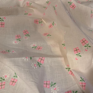 May include: White fabric with a repeating pattern of pink flower pots and white daisies with green stems and leaves. The fabric is wrinkled, creating shadows and depth. The overall theme is floral and vintage.