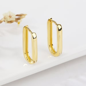 May include: A pair of gold hoop earrings with a rectangular shape. The earrings are simple and elegant.