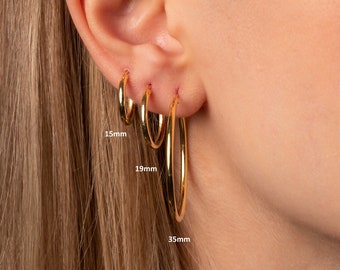 May include: Three gold hoop earrings of different sizes. The smallest hoop is 15mm, the middle hoop is 19mm, and the largest hoop is 35mm.