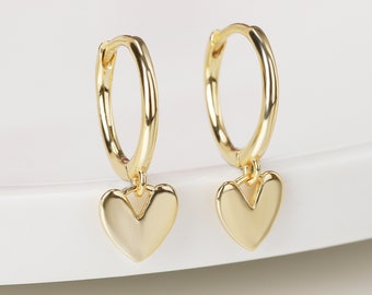 May include: Gold hoop earrings with a small heart charm dangling from each hoop.