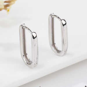 May include: A pair of silver hoop earrings with a rectangular shape. The earrings are made of metal and have a polished finish.
