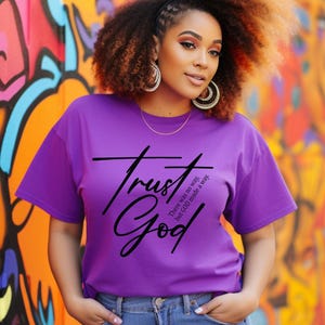 May include: A purple t-shirt with the text "Trust God" in black script. The text is accompanied by the phrase "There was no way, but God made a way."