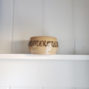 May include: A brown ceramic bowl with a geometric pattern around the rim. The bowl is sitting on a white shelf.