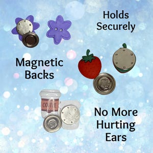 May include: A collection of decorative magnetic accessories featuring a purple flower, a red strawberry, and a white coffee cup. Each item has a circular magnetic back. Text on the image reads: Holds Securely, Magnetic Backs, No More Hurting Ears.