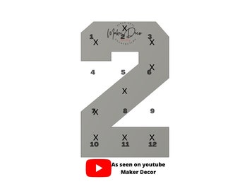 May include: A gray number two with twelve numbered squares marked with an X. The number two is outlined in black and has a Maker Decor logo in the top left corner. The text "As seen on youtube Maker Decor" is below the number.