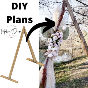 May include: DIY plans for a wooden archway, shown with a floral arrangement. The archway is made of two pieces of wood that are joined together at the top to form a triangle. The archway is decorated with flowers, greenery, and pampas grass.