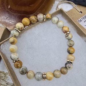 May include: A bracelet made of yellow, brown, and white agate beads with gold accents. The bracelet is on a white background.