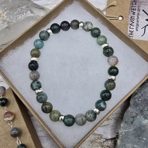 May include: A green, gray, and white agate gemstone bracelet with silver spacers. The bracelet is in a small, brown box with a tag that reads "The Gypsy Witch Unique Handmade Gifts".