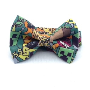 May include: A colorful bow tie featuring a pixelated design with green, yellow, orange, and brown elements. The bow tie has a repeating pattern with the word "TNT" and a pixelated face.