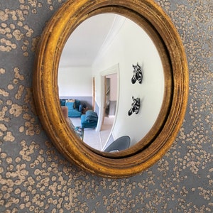 Pu&ograve; includere: Uno specchio rotondo con cornice dorata, che riflette una stanza con pareti bianche e un tappeto a motivi. Due decorazioni murali a forma di testa di zebra in bianco e nero sono visibili nel riflesso.